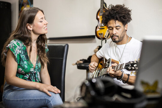 Girlfriend singing while sitting by boyfriend playing guitar during rehearsal at home