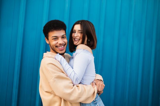 Happy young couple embracing each other while standing against blue wall