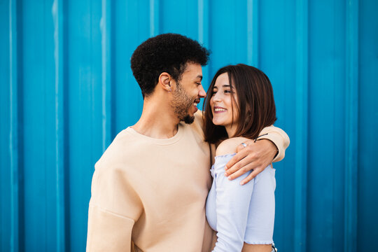 Smiling young man embracing woman while standing against blue wall