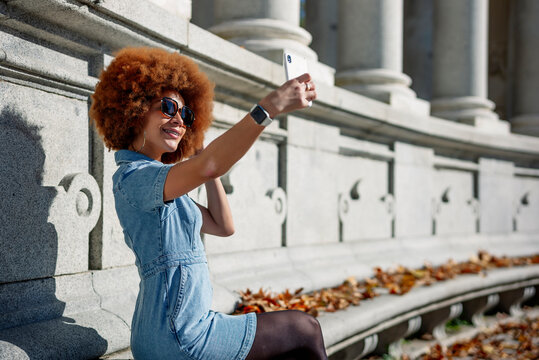 Smiling woman taking selfie at Alfonso Xii Monument on sunny day, Parque Del Buen Retiro, Spain