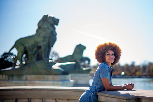Smiling woman leaning on railing against statue during sunny day at Estanque Grande Del Retiro pond, Spain