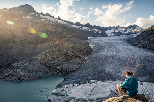Switzerland, Valais, Obergoms, Man sitting on rock, overlooking Rhone Glacier and mountains