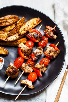 Gyros spiced chicken skewers with tomatoes, bell peppers, potato wedges on table