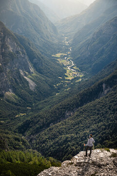 Woman with hiking poles standing on rock and looking at valley