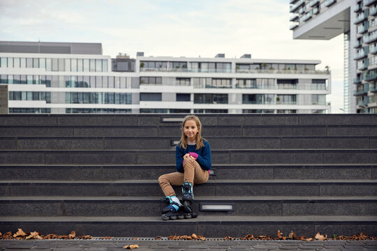 Girl wearing roller skate smiling while sitting on staircase in city