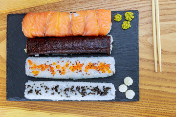 Sushi roll with salmon, red caviar and black caviar on a black plate on a wooden surface.