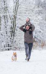 Fototapeta na wymiar Father and a little baby girl playing in the snow with a welsh corgi pembroke dog