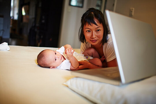 Mother and baby son lying on bed with laptop