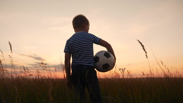 Childhood dream. boy holding soccer ball walking in the park silhouette. happy family kid dream concept. kid boy walking on the field silhouette at sunset carries a soccer fun ball. baby winner