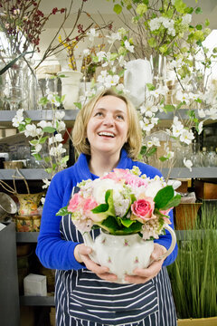 Floral designer holding teapot flower arrangement in studio