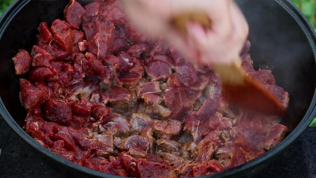 cooking process of an oriental dish. red meat boils and stews in oil in a large pot. large traditional Asian cauldron on an open fire, called a Kazan