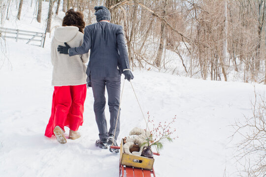 Mid adult couple walking through snowy field, man pulling sled, rear view