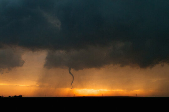 West of Larned, Kansas, USA, a tornado forms from a storm's wall cloud against golden sunset, 18 May 2013