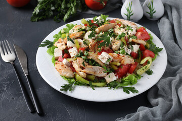 Salad with bulgur, baked chicken, bell pepper, basil and feta on white plate on dark background, Closeup. Horizontal format