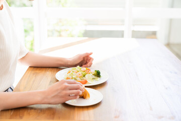 Obraz na płótnie Canvas サラダとクロワッサンを食べる女性　手元