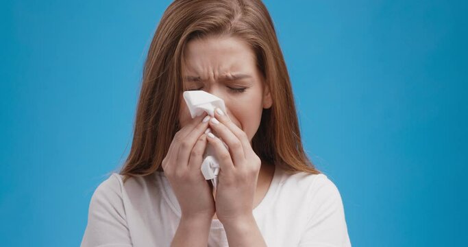 Studio portrait of young sick lady blowing her nose, blue background, slow motion