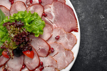 Cold cuts thinly sliced, sausage, bacon, boiled pork, meat, with lettuce, basil, cherry tomatoes and pomegranate seeds, on a white plate