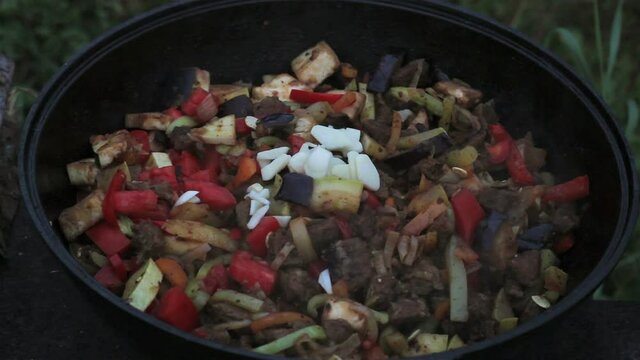 put eggplants in a big pot with meat, onions, carrots, zucchini. all ingredients are mixed with a wooden spatula. cooking on open fire