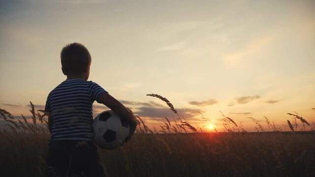 Childhood dream. boy holding soccer ball walking in the park silhouette. happy family kid dream concept. kid boy walking on the field silhouette at sunset carries fun a soccer ball. baby winner