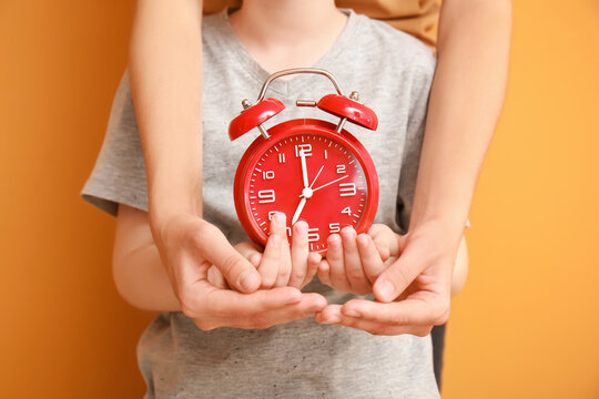 Hands of family with alarm clock on color background