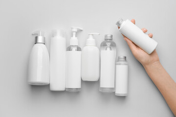 Female hand with cosmetic bottles on light background
