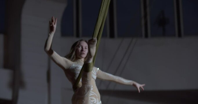 Agile woman in white costume is doing a split in the air, aerial silks, circus
