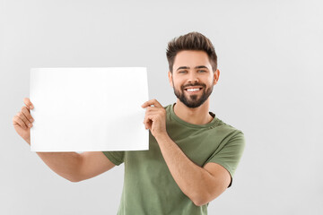 Young man with blank paper sheet on light background