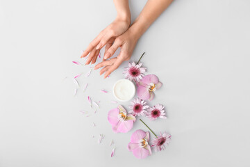 Obraz na płótnie Canvas Female hands with cream and beautiful flowers on light background