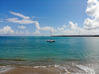 A double hulled sailboat anchored in blue green waters along shoreline in the Dominican Republic, with lapping ocean waves in foreground