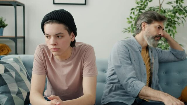 Slow motion portrait of miserable people kid and dad sitting on couch not talking feeling sad having family problem and misunderstanding. House and emotions concept.