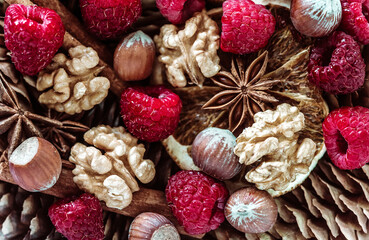 spices and berries on a gray background. spices for mulled wine, raspberries and nuts on the background of cones. still life with cones, fresh raspberries, nuts and spices for drinks