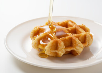 Dripping honey on waffles placed on a white background