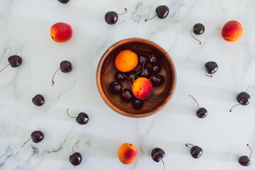 Naklejka na ściany i meble simple food ingredients, fresh apricots and cherries on marble background with wooden bowl