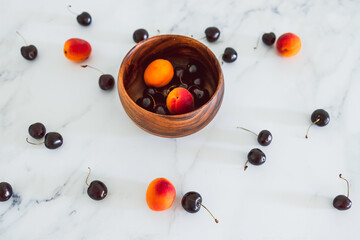 simple food ingredients, fresh apricots and cherries on marble background with wooden bowl