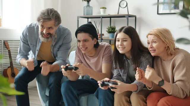 Teenage boy and girl playing video game doing high-five with parents and hugging enjoying modern technology and leisure time activity during self-isolation