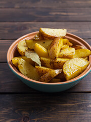 Slices of baked potatoes with herbs in a plate on a wooden table. Horiz. Vertical orientation, no people, copy space, close-up