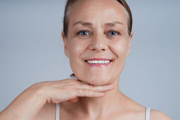 An adult smiling woman touches her chin with her palm, applies a lifting effect cream.