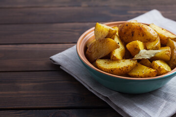 Slices of baked potatoes with herbs in a plate on a kitchen towel and a wooden table. Horizontal orientation, no people, copy space, close-up