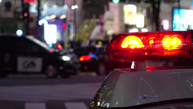 SHIBUYA, TOKYO, JAPAN - JAN 2021 : View of Police car with red beacon light at night downtown city. Crowd of people and street traffic at Shibuya crossing in background. Crime and emergency concept.