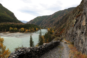 Mountain trail with a stone wall at a cliff face overlooking the confluence of turquoise mountain...