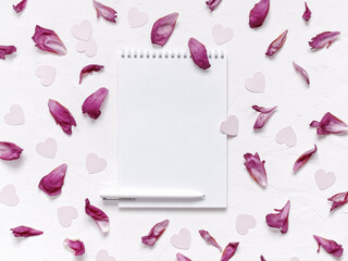 Open blank notebook, pen, peony petals, heart-shaped confetti are on a textured background. Floral layout for Valentine's day. Flat lay. Top view. Copy space.