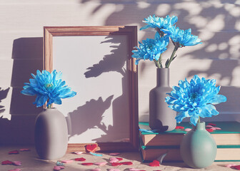 Empty wooden photo frame, blue chrysanthemums in vases, shapes in the form of hearts are on a light wooden background. Floral template for valentine's day, mother's day. Copy space.