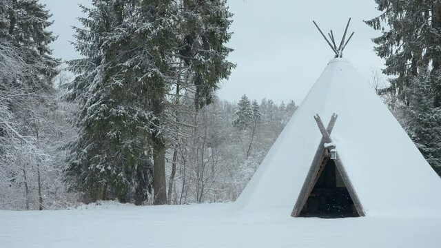 The teepee covered in thick white snow in the forest with the trees on the back filled with snow