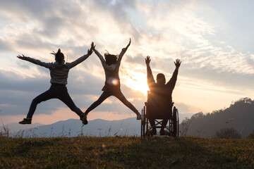 Silhouette happy disabled woman sitting on her wheelchair. her daughters stretching hands jumping...