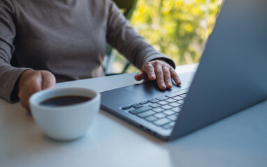 Closeup image of a woman working and touching on laptop computer touchpad while drinking coffee