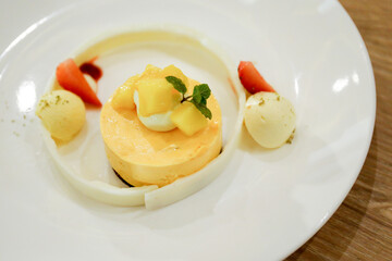 Mango dessert and sour cream parfait dessert topped with slices of mango on a plate decorated with mango puree. Pastel yellow cheesecake colors