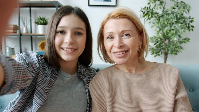 Portrait of mother and daughter looking at camera waving hand and talking through video call at home. Modern communication and social distancing concept.