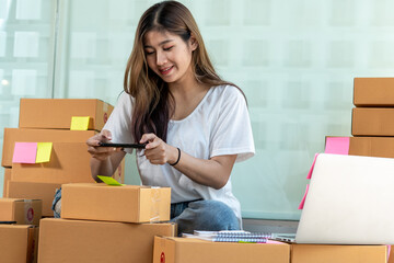 The Asian owner takes pictures of a brown package to verify his customer's address and make arrangements for delivery online while he works at home.