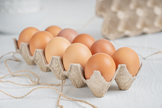 Raw brown dozen fresh chicken eggs in opened box made of recycled paper on white wooden background at kitchen. Healthy eating and sustainable consumption concept. Horizontal orientation image
