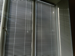 White horizontal blinds on the window block out the bright sunlight.